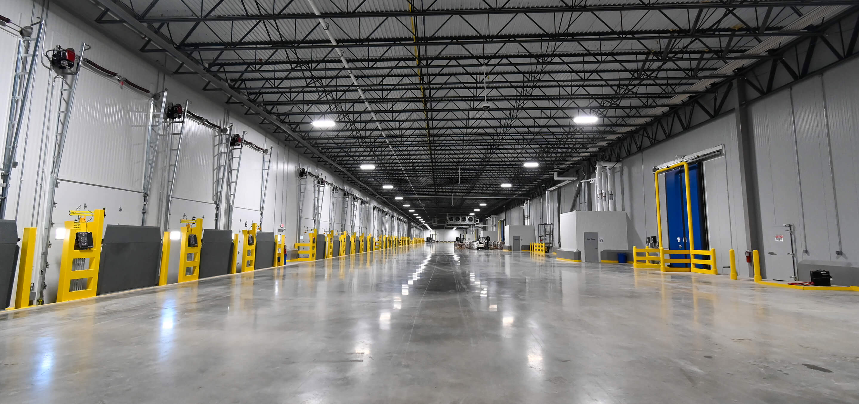 Interior of modern cold storage warehouse with high ceilings, LED lighting, yellow safety barriers, and polished concrete floors showing controlled temperature environment